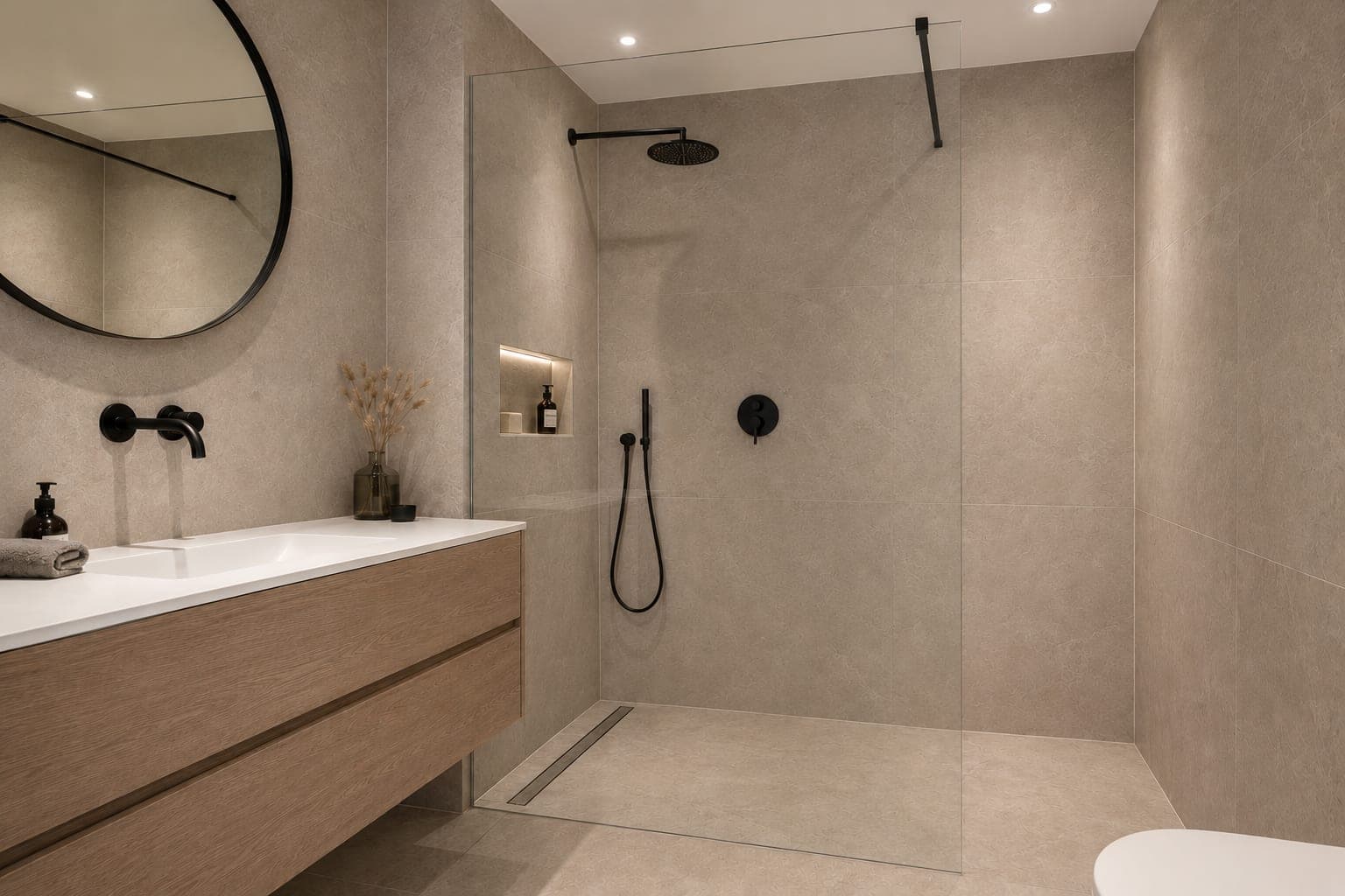 Badkamer met een inloopdouche achter glas, een ronde spiegel en een houten wastafelmeubel, in beigegrijze tegels.