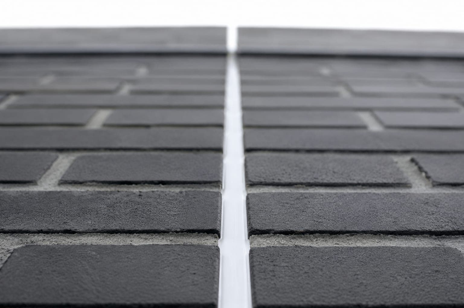 Antracietgrijze bakstenen gevel van dichtbij, met een rechte lichtgrijze kitvoeg die verticaal door het metselwerk loopt.