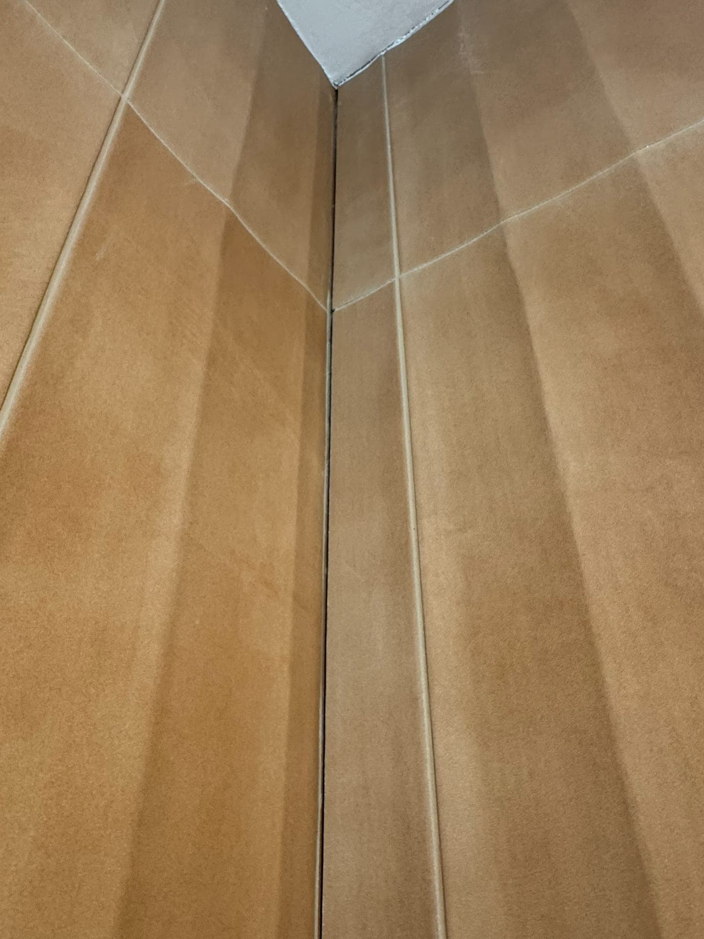 Strakke verticale kitnaad in de hoek tussen twee okerkleurige tegelwanden.