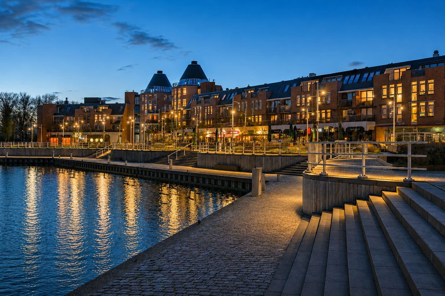 Woningen met verlichte ramen langs een kade in de avondschemering, met de lantaarns weerspiegeld in het water.
