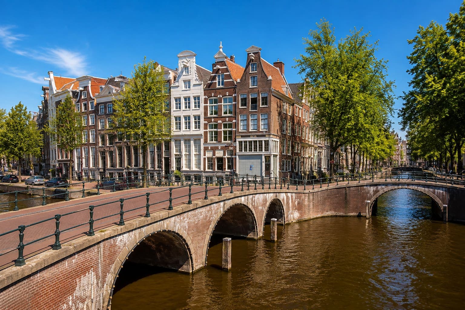 Amsterdamse gracht met een gemetselde boogbrug op de voorgrond en een rij grachtenpanden met trap- en klokgevels erachter.