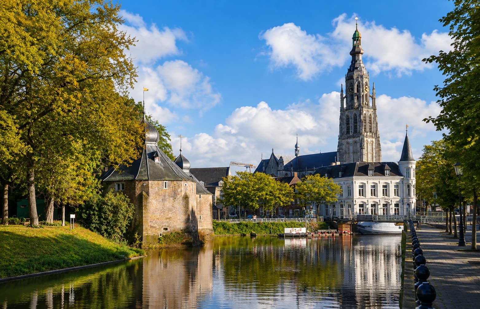 Water met links een oude ronde verdedigingstoren van baksteen, en daarachter de hoge toren van de Grote Kerk in Breda.