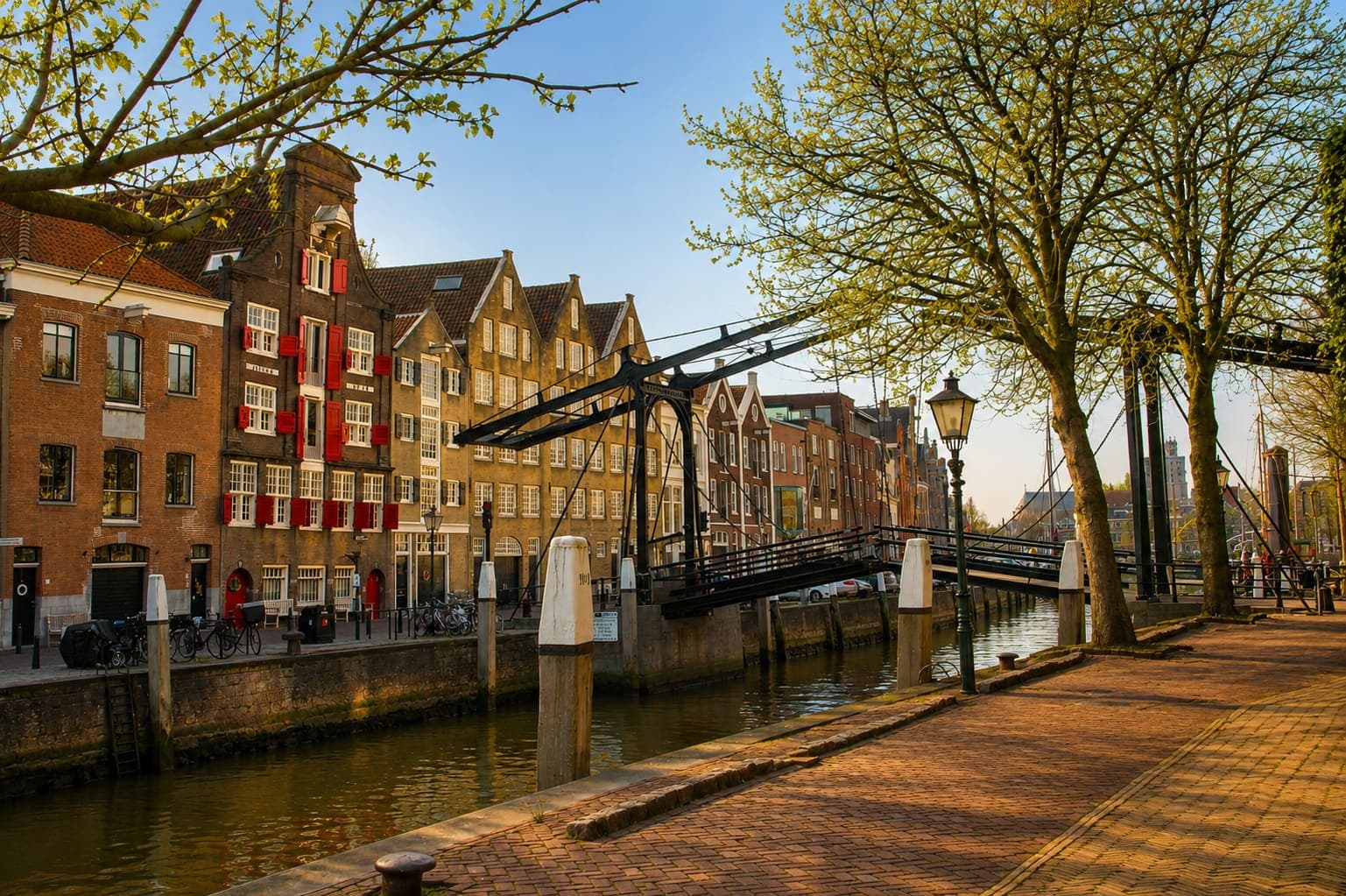 Gracht met bakstenen pakhuizen met rode luiken, een stalen ophaalbrug en een gemetselde kade met lantaarns.