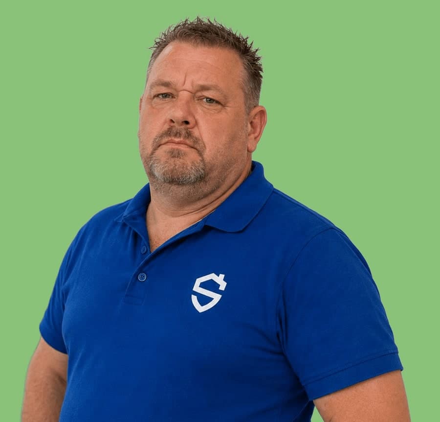 Man met kort haar en een baardje in een blauwe bedrijfspolo, op een effen groene achtergrond.
