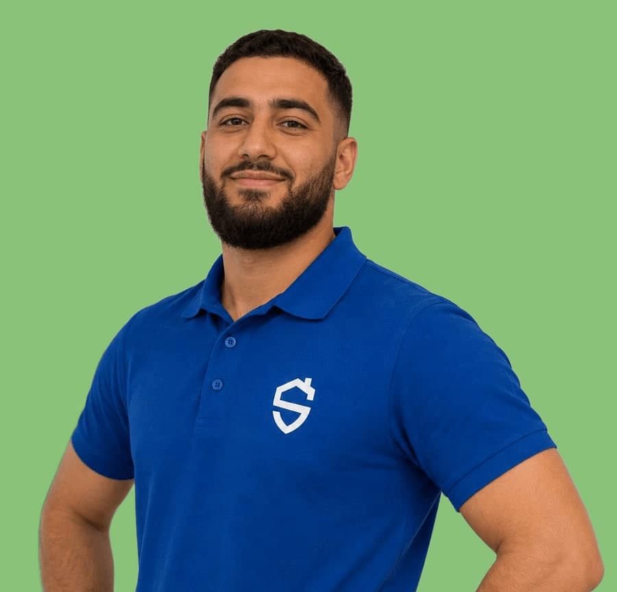 Man met baard in een blauwe bedrijfspolo, handen in de zij, op een effen groene achtergrond.