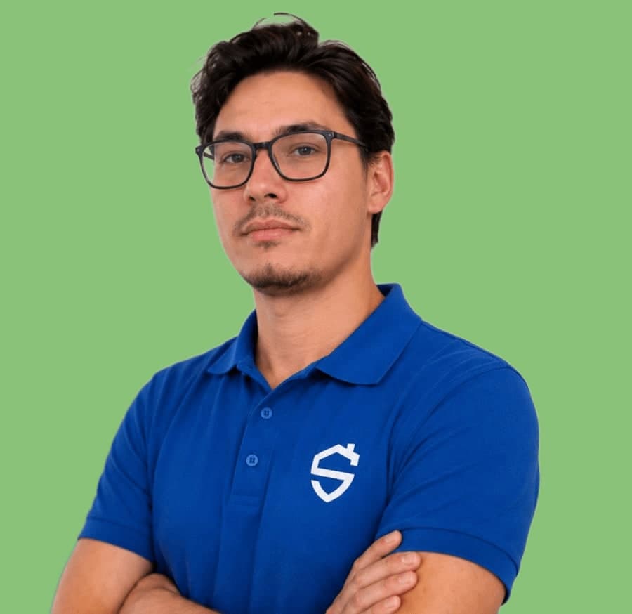 Man met bril in een blauwe bedrijfspolo, armen over elkaar, op een effen groene achtergrond.